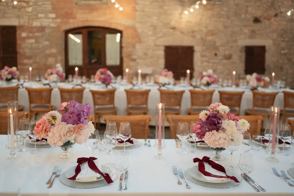 Wedding table with pink flowers, candles and velvet ribbons in a stone courtyard